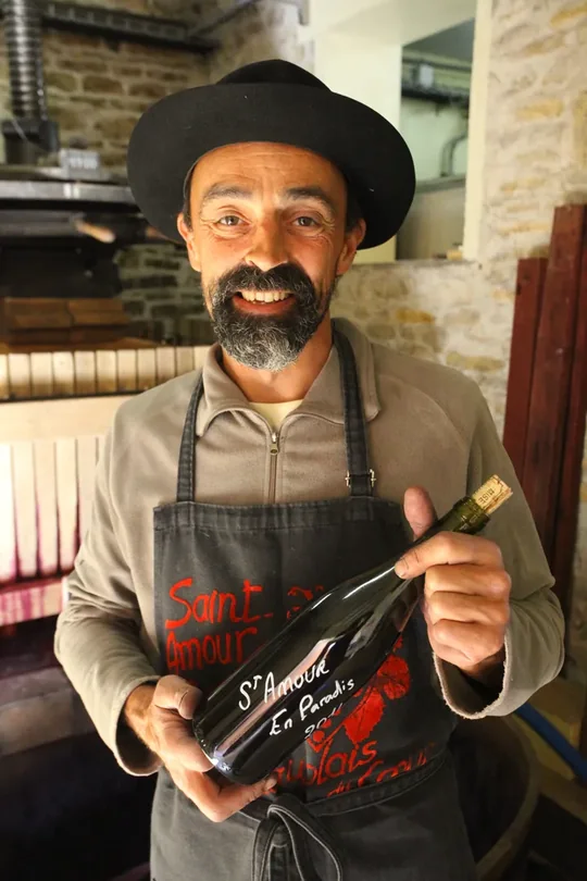 Pascal Durand, vigneron, devant son pressoir, tenant une bouteille de Saint-Amour « En Paradis »